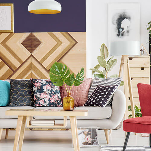Room with many colors and designs with couch, chair, table, lamp, paintings, and potted plants
